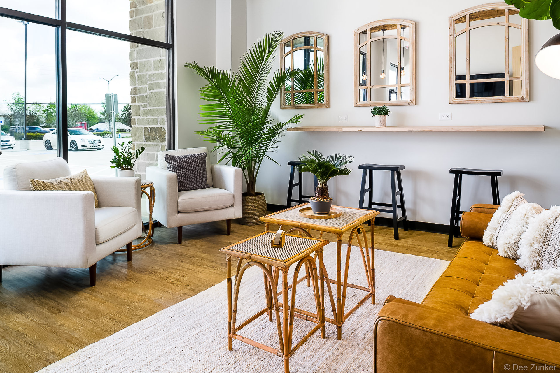 Bright dental office waiting room with rattan tables, white armchairs, leather sofa, tropical plants, and arched mirrors, Houston TX.