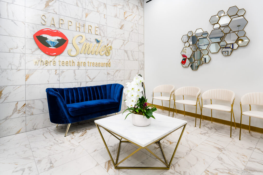 Luxury dental office reception area with blue velvet sofa, marble floors, gold accents, and branded wall signage in Houston, TX.