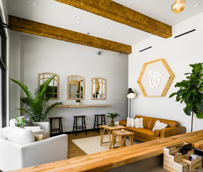 Warm dental office waiting room in Stafford TX featuring wood beam ceiling leather sofa rattan tables and tropical plants