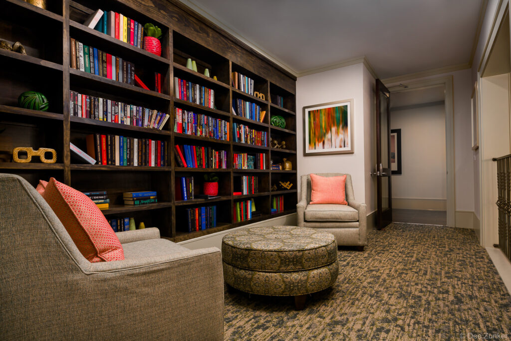 Cozy apartment library nook with floor-to-ceiling bookshelves, two armchairs, and patterned ottoman in Energy Corridor Houston
