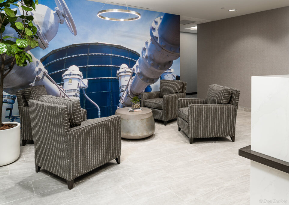 Renovated engineering office lobby featuring dark striped armchairs arranged around a concrete coffee table with an industrial pipe mural accent wall