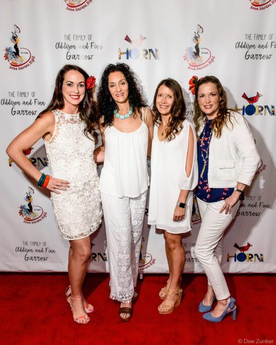 Four women in white attire posing on the red carpet at a Houston gala event, photographed by Dee Zunker Photography