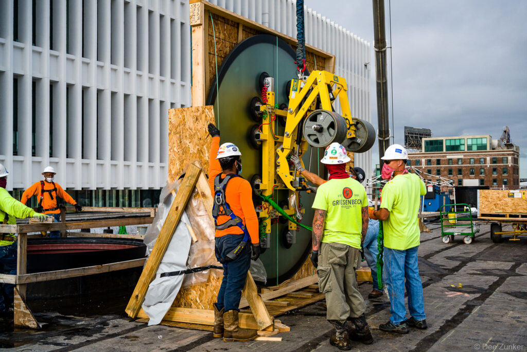 Construction crew using vacuum lift equipment to install large curved glass panel at Post HTX commercial project in Houston, TX.