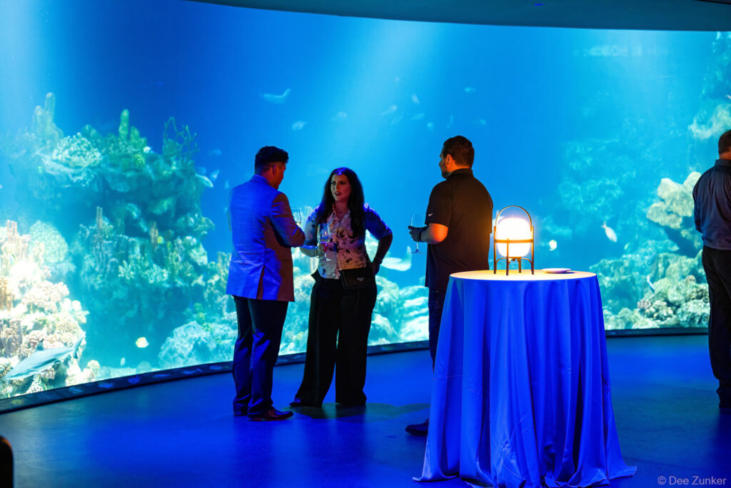 Corporate event attendees networking beside a large aquarium display at the Gulf Coast Green reception in Houston.