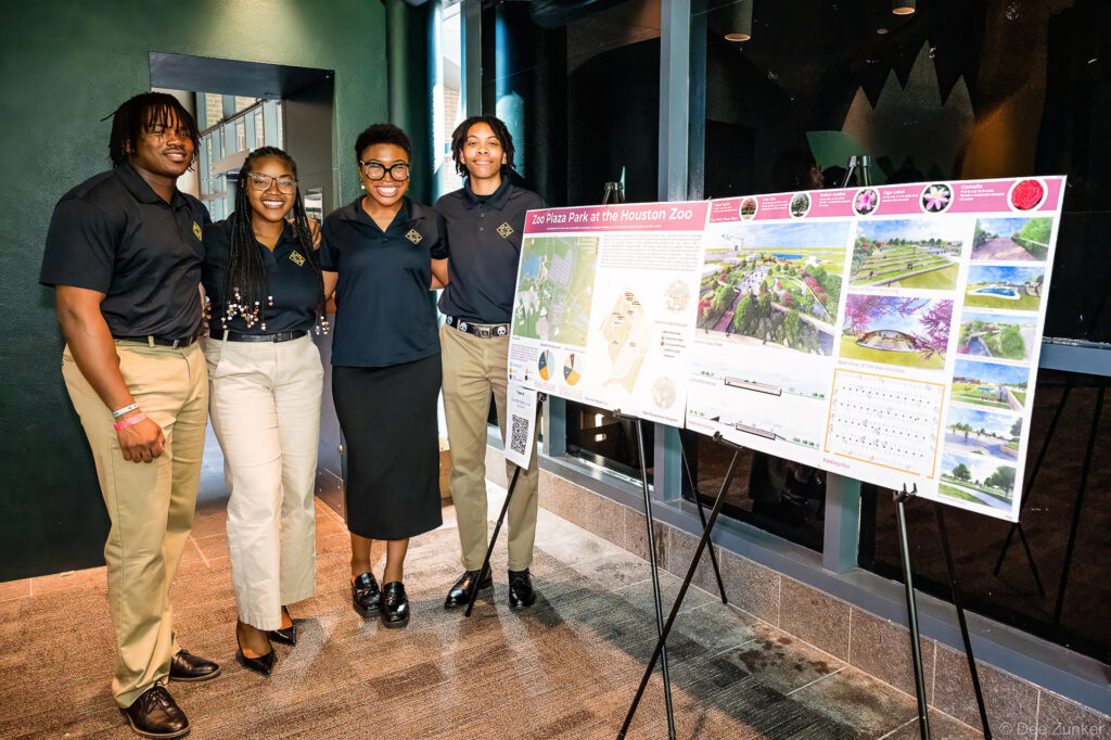 Four students in matching uniforms pose beside a Zoo Plaza Park at the Houston Zoo landscape architecture presentation board at Gulf Coast Green conference.