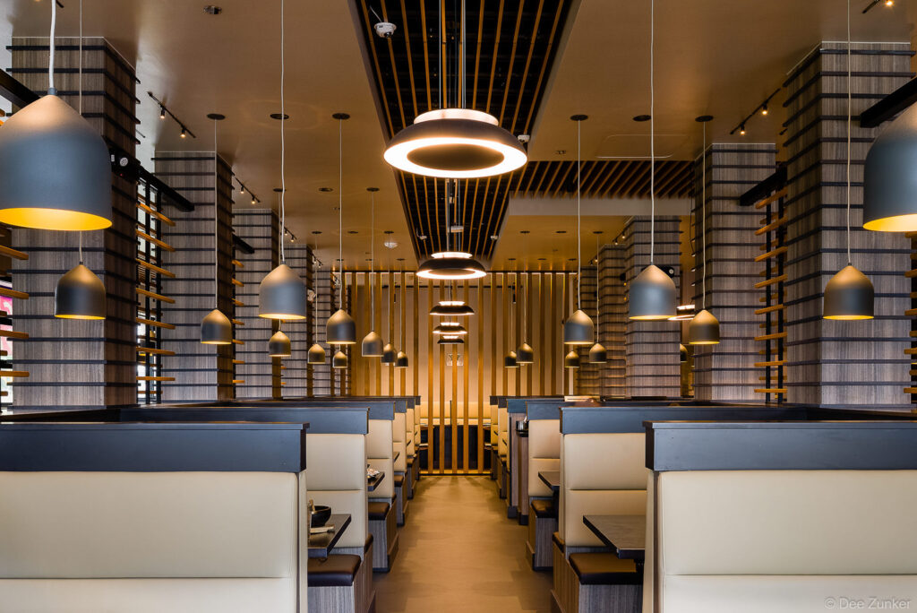 Symmetrical Japanese BBQ restaurant dining room with cream leather booths, pendant lights, and wood slat columns in Houston.