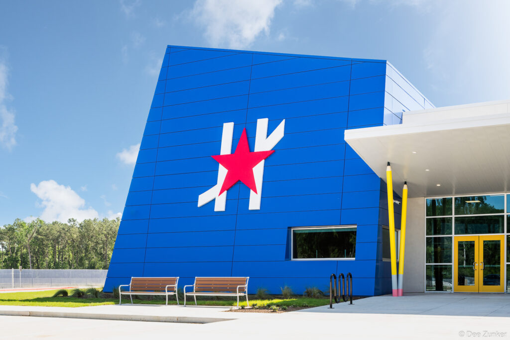 Exterior of a bold blue school building in Spring TX featuring oversized pencil sculptures and a red star logo near the entrance