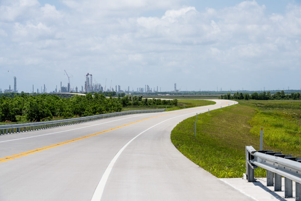 Newly paved Highway 99 Grand Parkway curves through flat Texas landscape with petrochemical refineries visible on the horizon.