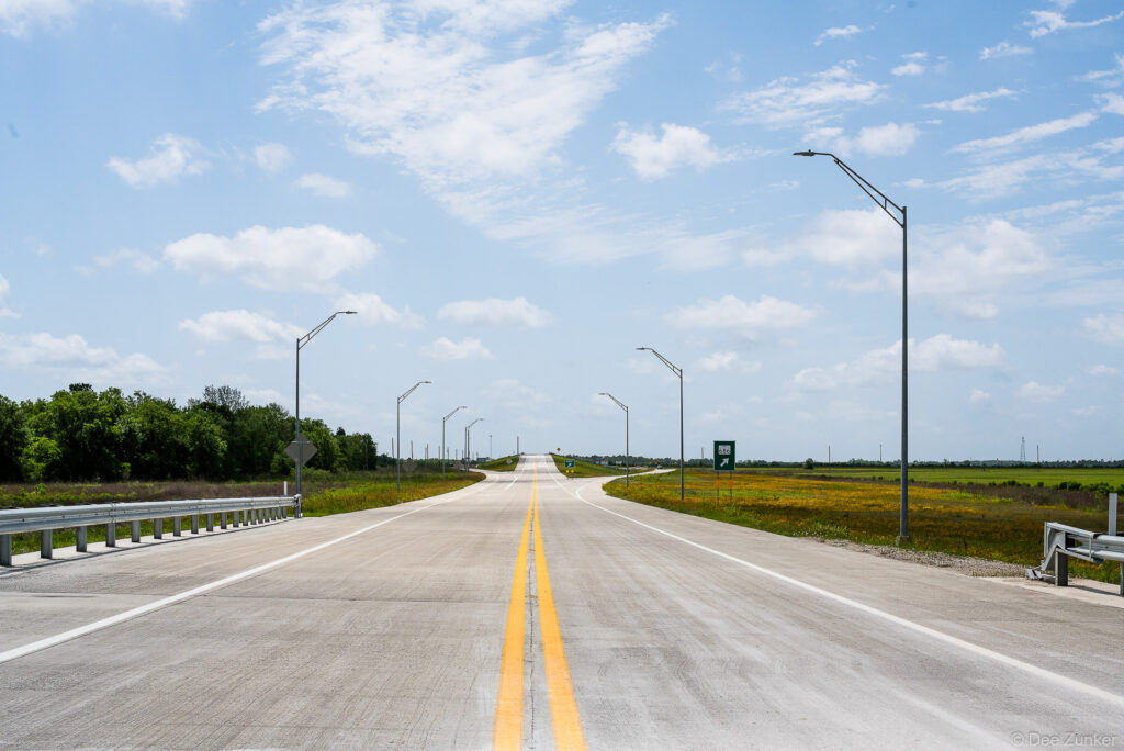 Newly completed concrete highway with double yellow centerline, street lights, and open fields along Highway 99 Grand Parkway near Houston, TX.