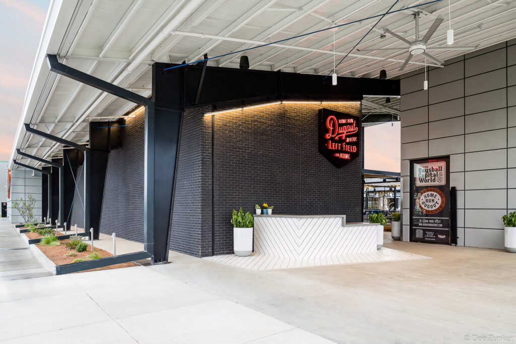 Exterior entrance of a baseball-themed entertainment venue in Katy TX featuring neon signage dark brick and a modern reception desk
