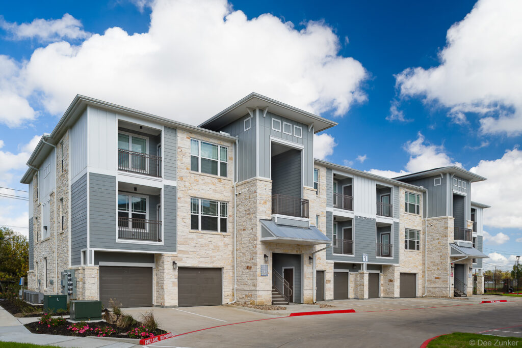 Three-story Houston apartment exterior featuring limestone and gray board-and-batten siding with private garages and balconies