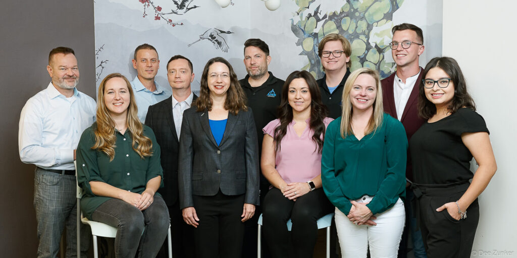 Eleven architecture firm professionals pose together for a corporate group photo in a Houston office with decorative wall mural.