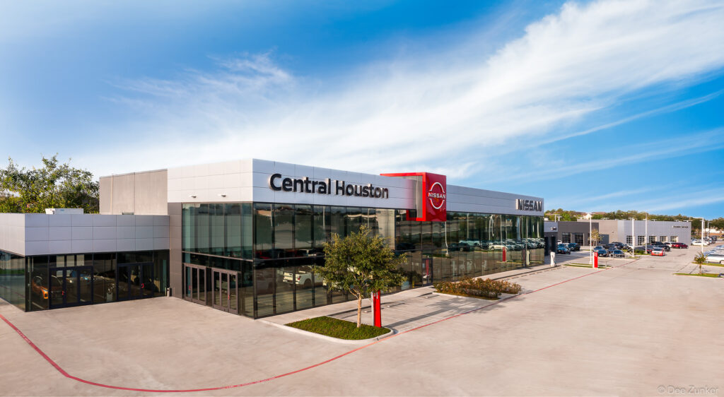 Exterior architectural photography of a Houston automotive dealership showroom featuring floor-to-ceiling glass facades and modern design