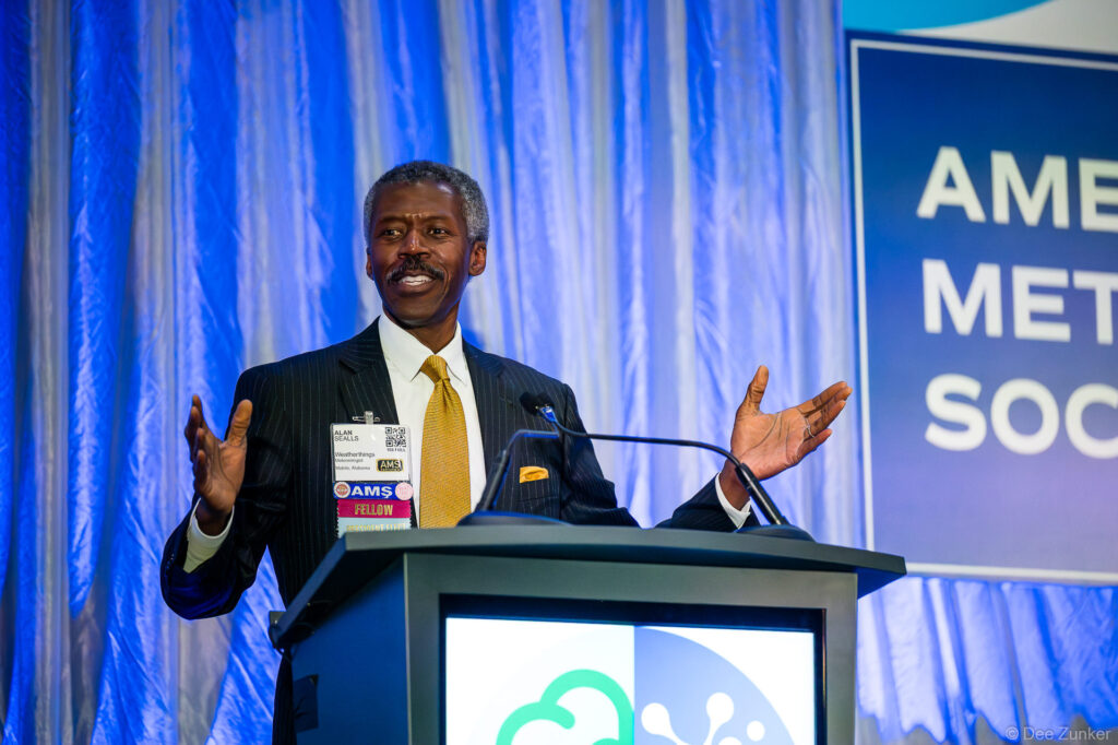 Keynote speaker at Houston awards ceremony gestures expressively at podium before professional meteorological society audience