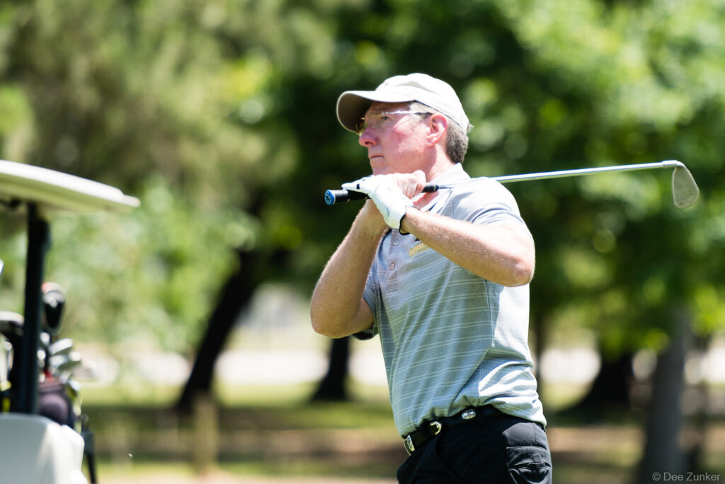 Golfer in follow-through pose holding iron club at Houston corporate golf classic charity tournament event.