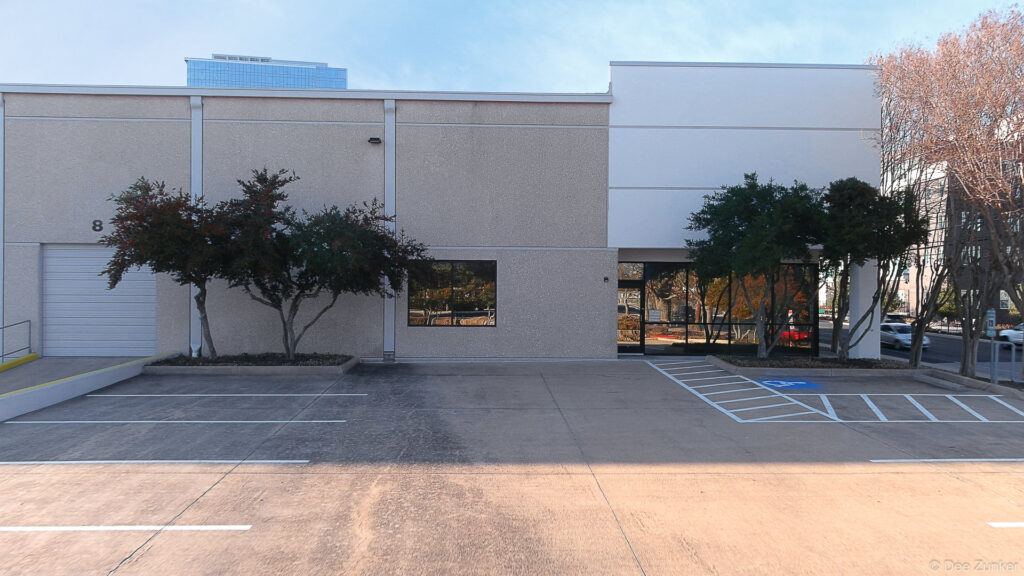 Exterior facade of a single-story commercial office building with parking lot and accessible parking space in Houston, TX.