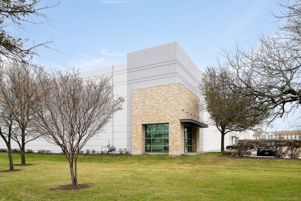 Modern tilt-wall commercial warehouse exterior with limestone facade entry, glass doors, and landscaped grounds in Houston, TX.