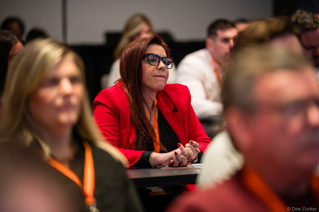 Female conference attendee in red blazer listens attentively during a Houston corporate event session