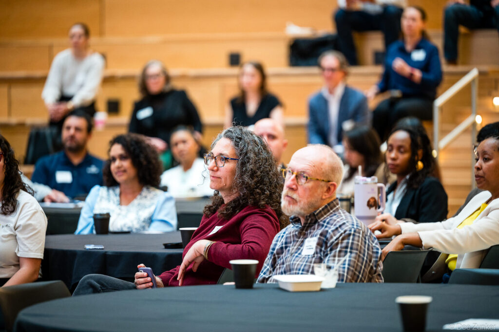 Diverse conference attendees seated at round tables listening attentively during a Houston corporate event in a modern auditorium