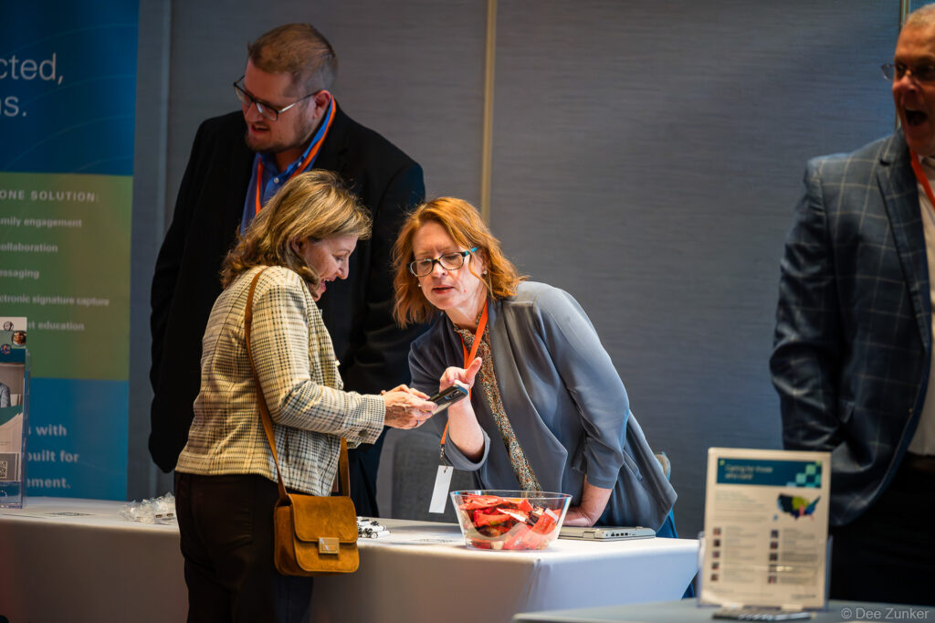 Conference exhibitor booth staff demonstrating product to attendee on smartphone at Houston corporate event