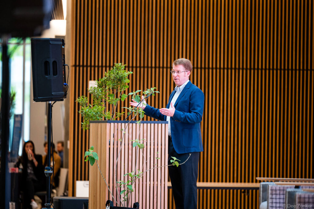 Male conference speaker in navy blazer presenting at a modern wood-paneled podium during the Gulf Coast Green Houston event