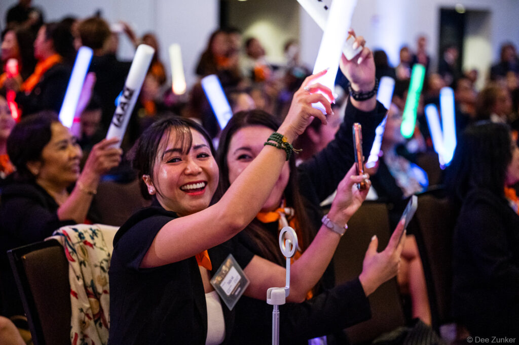 Smiling conference attendees wave glowing LED sticks during a Houston corporate event celebration in a packed ballroom