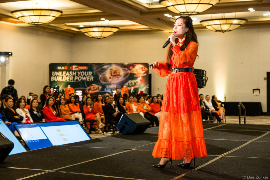 Woman in red lace gown performing on stage with microphone at Houston corporate event before seated audience