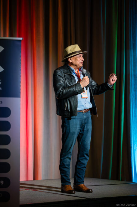 Male keynote speaker in leather jacket and hat addresses corporate conference audience from stage, Houston event photography