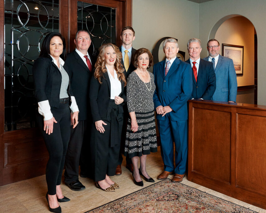 Eight professionally dressed corporate team members pose together in an upscale Houston office lobby for a group portrait photo.
