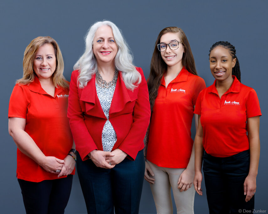Four professional women in red branded polo shirts pose together for a corporate group portrait, Houston healthcare company team photo. Composite group shot.