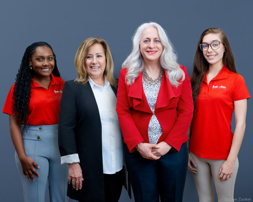 Four professional women in red and black attire pose together for a corporate group portrait, Houston healthcare company team photo. Composite group shot.