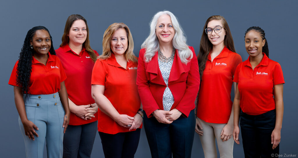 Six women in red uniforms and blazer pose together for a corporate group photo for a Houston healthcare company. Composite group shot.