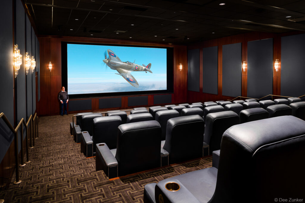 Luxury private home theater with black leather recliner seats, large projection screen displaying a WWII Spitfire aircraft, Houston interior architecture photography