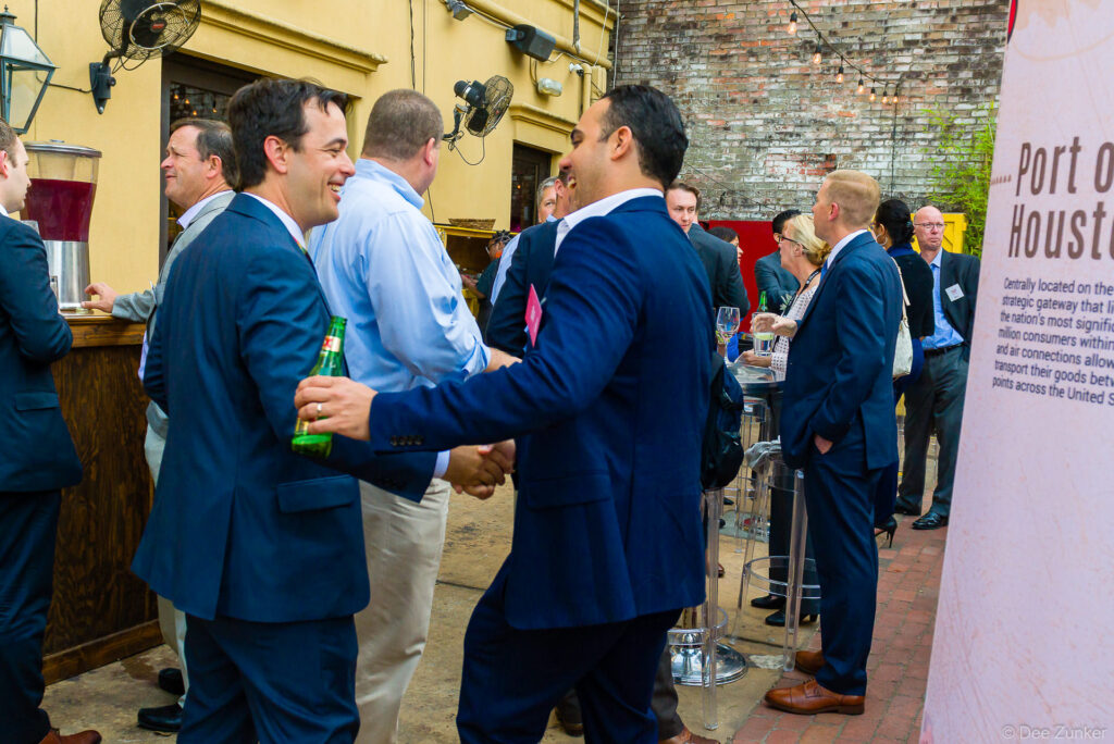 Business professionals in suits shaking hands and networking at an outdoor corporate reception event in Houston, TX.