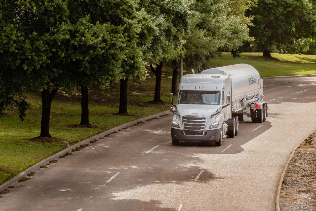 White cryogenic tanker semi-truck navigating a tree-lined road, Houston industrial transportation photography by Dee Zunker.