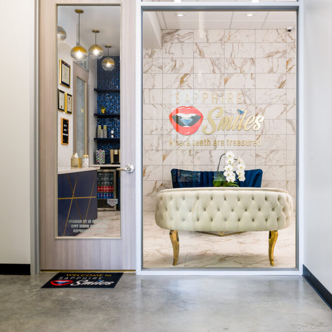 Elegant dental office reception area with tufted ivory bench, marble accent wall, gold signage, and blue cabinetry in Houston, TX.