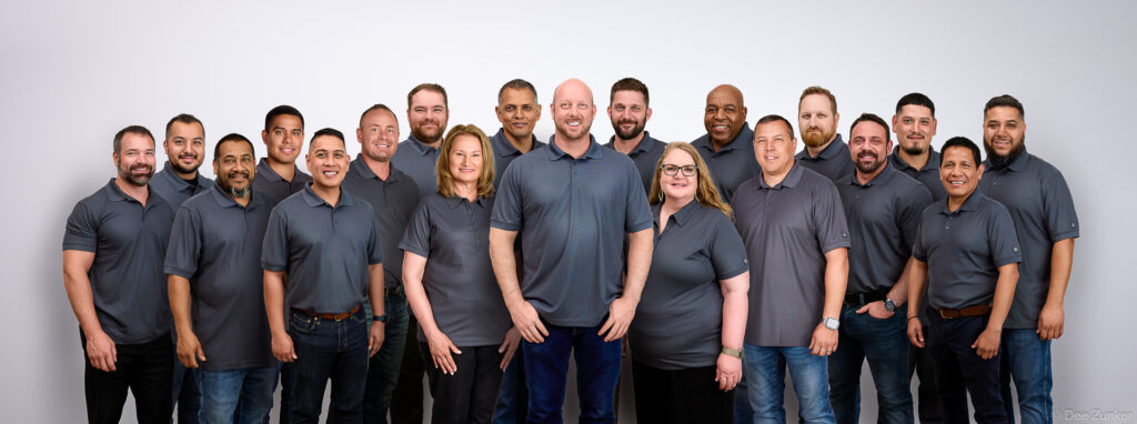 Large corporate group of approximately 20 employees in matching grey polo shirts posed for a professional team photo in Houston. Composite group shot.