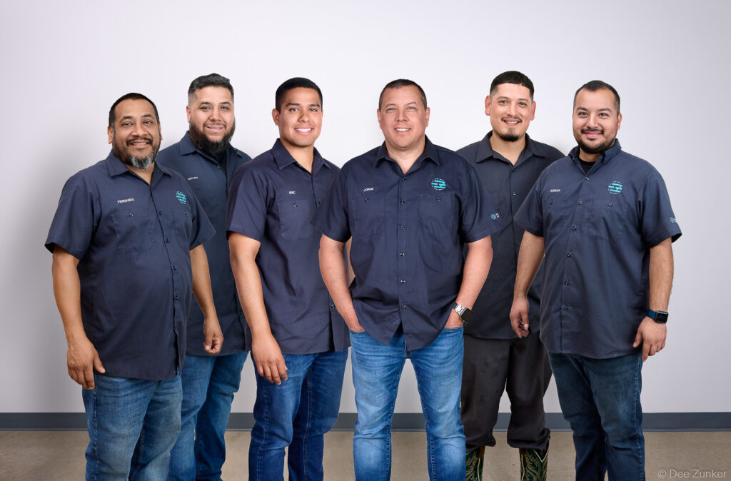 Six male employees in matching navy uniforms pose for a corporate group photo for a Houston drilling company. Composite group shot.