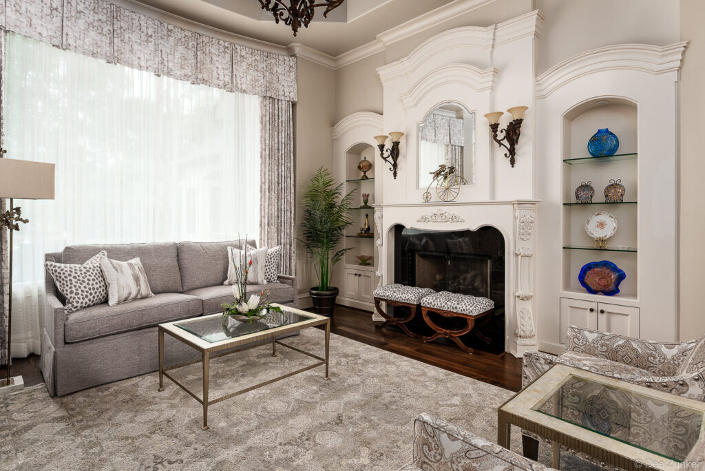 Formal Houston living room with white ornate fireplace, gray sofa, leopard print ottomans, built-in shelving, and tall windows with patterned drapes.