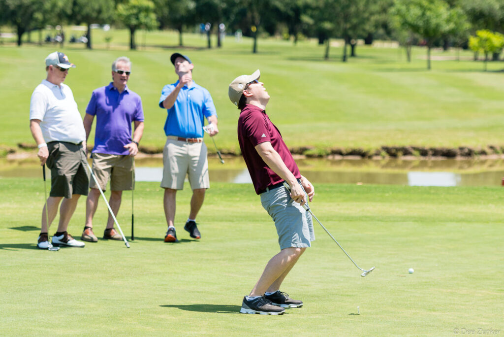 Golfer reacts with disappointment after missed putt on green, three fellow players watching, Houston corporate golf classic event.