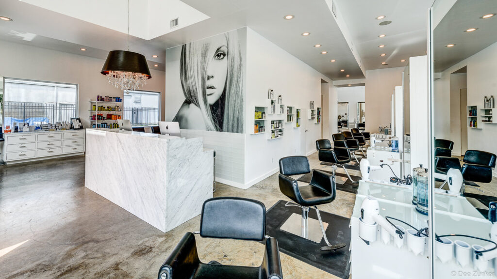 Modern Houston hair salon interior with marble reception desk, black styling chairs, and large black and white portrait mural