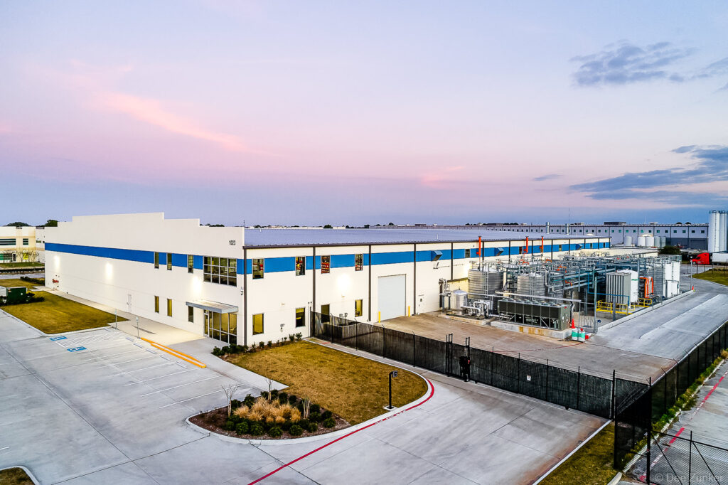 Aerial dusk view of a modern industrial facility with white and blue facade, outdoor processing equipment, and parking lot in Houston, TX.