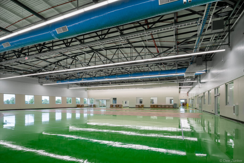 Spacious industrial warehouse interior with glossy green epoxy floor, exposed steel trusses, blue HVAC ducts, and bright LED lighting in Houston.