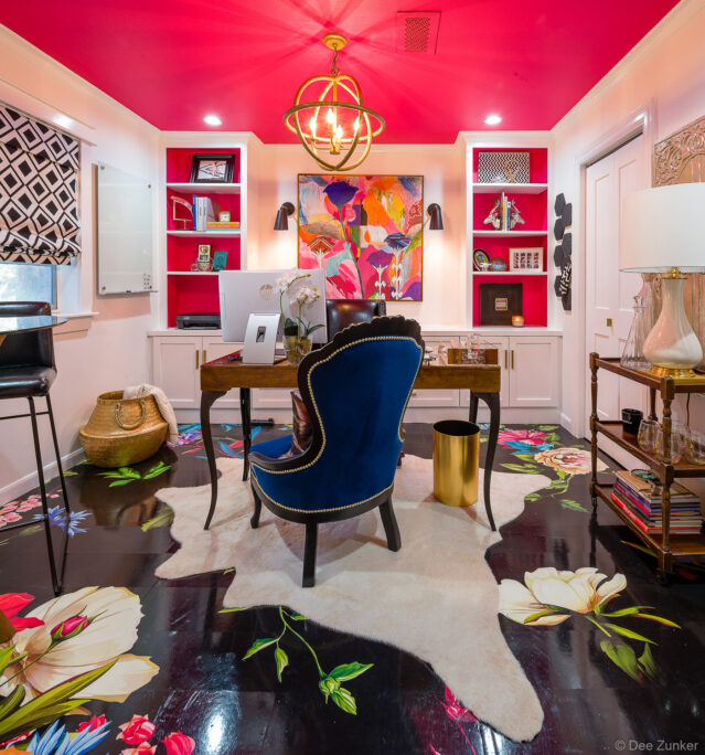 Bold home office with custom painted floral floor, pink ceiling, blue velvet chair, built-in shelving, and gold chandelier in Houston