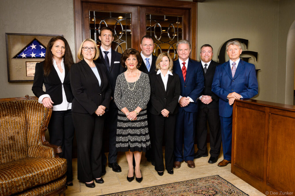 Nine professionally dressed attorneys and staff pose together in a wood-paneled Houston law firm lobby for a corporate group portrait.