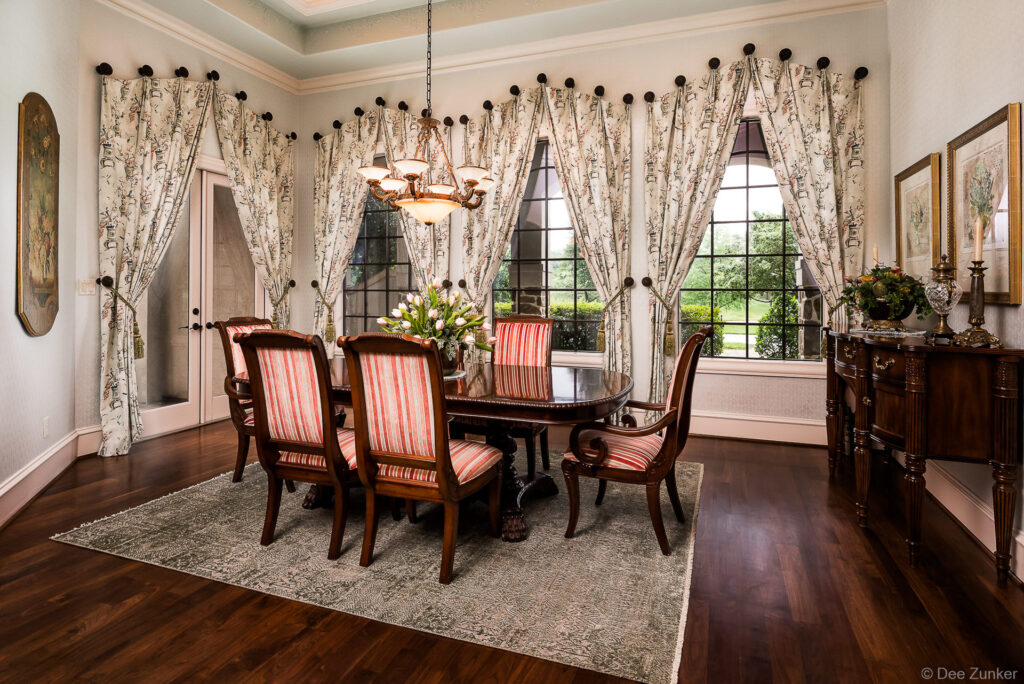 Formal dining room with dark wood furniture, striped upholstered chairs, floral curtains, and chandelier in a Houston luxury home.