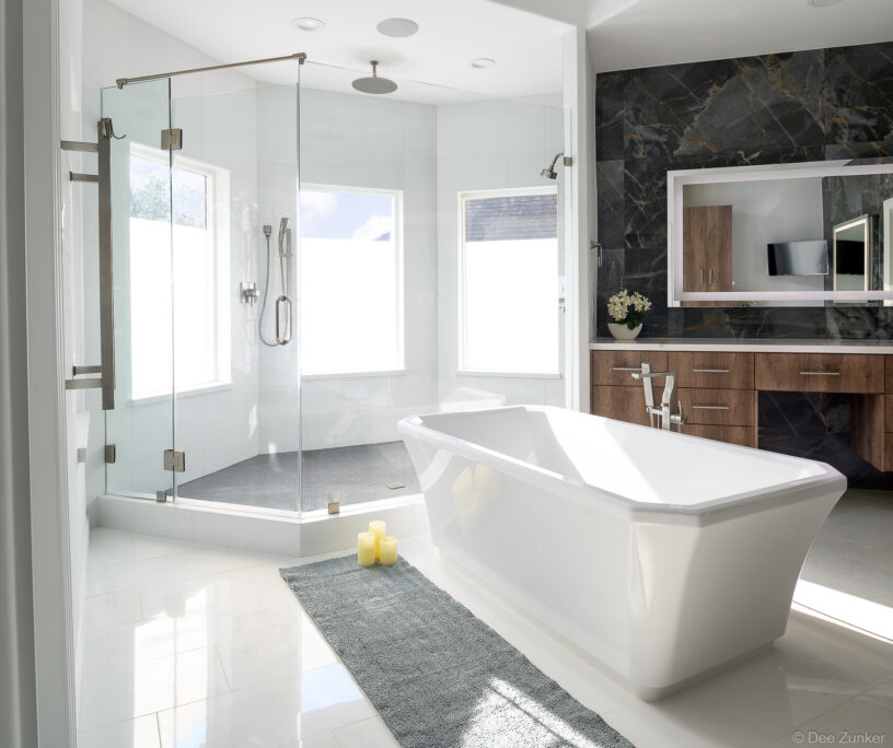 Modern Houston master bathroom with freestanding soaking tub, glass corner shower, dark marble accent wall, and warm wood vanity cabinetry.