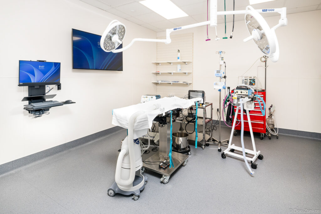 Bright modern operating room with surgical lights, draped table, anesthesia equipment, and wall-mounted monitors inside a Houston medical facility.