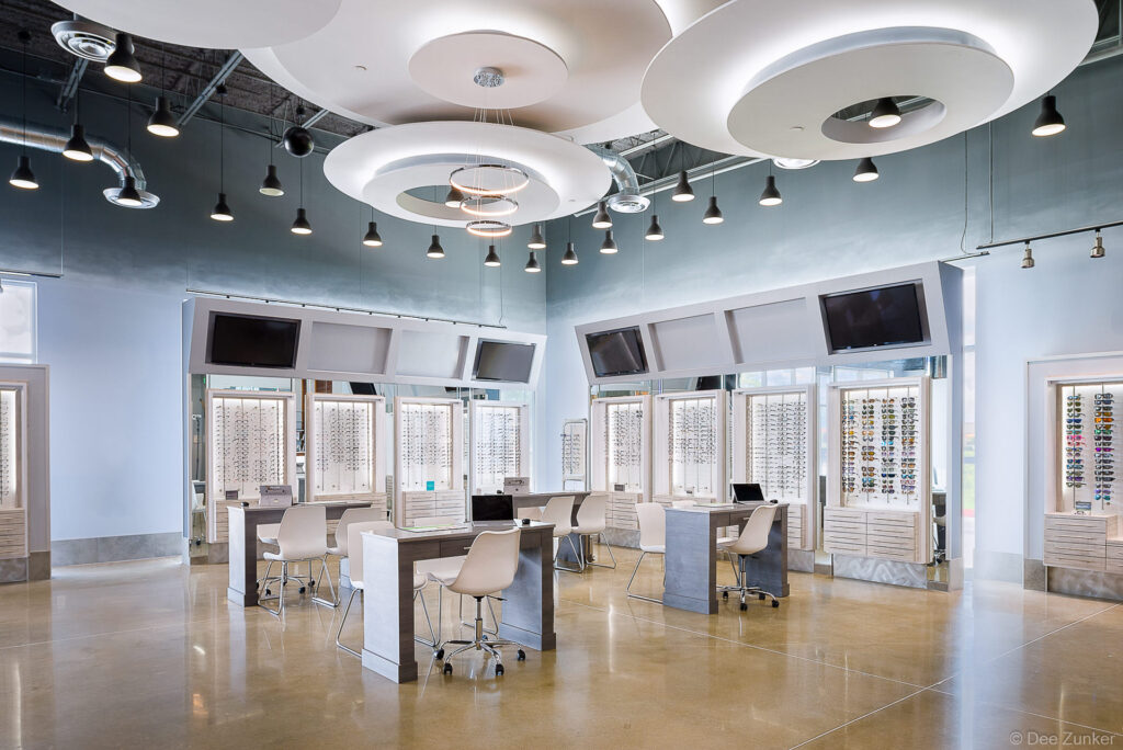 Bright Houston optical store interior with eyeglass display walls, workstation desks, pendant lighting, and modern circular ceiling features.
