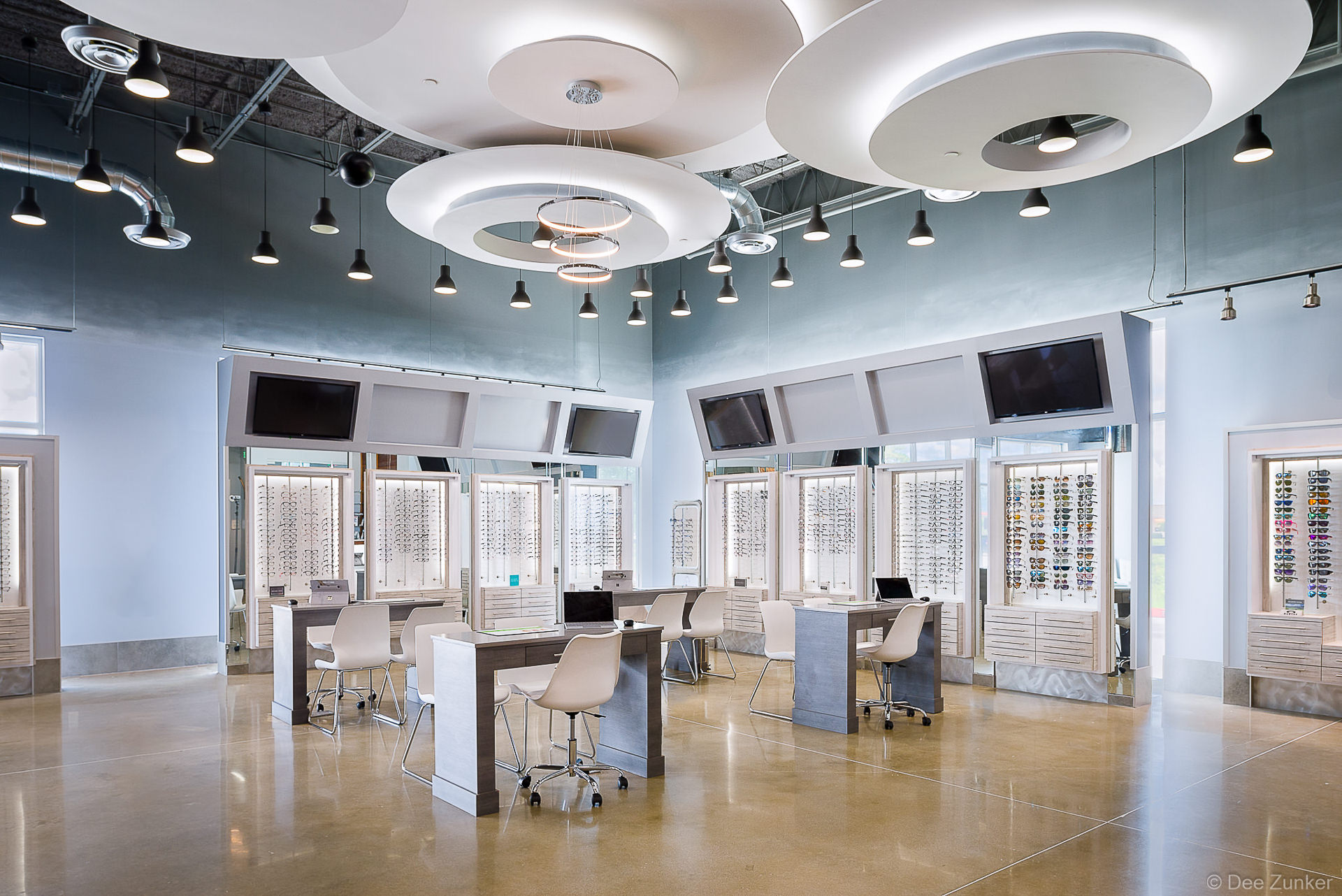 Bright Houston optical store interior with eyeglass display walls, workstation desks, pendant lighting, and modern circular ceiling features.